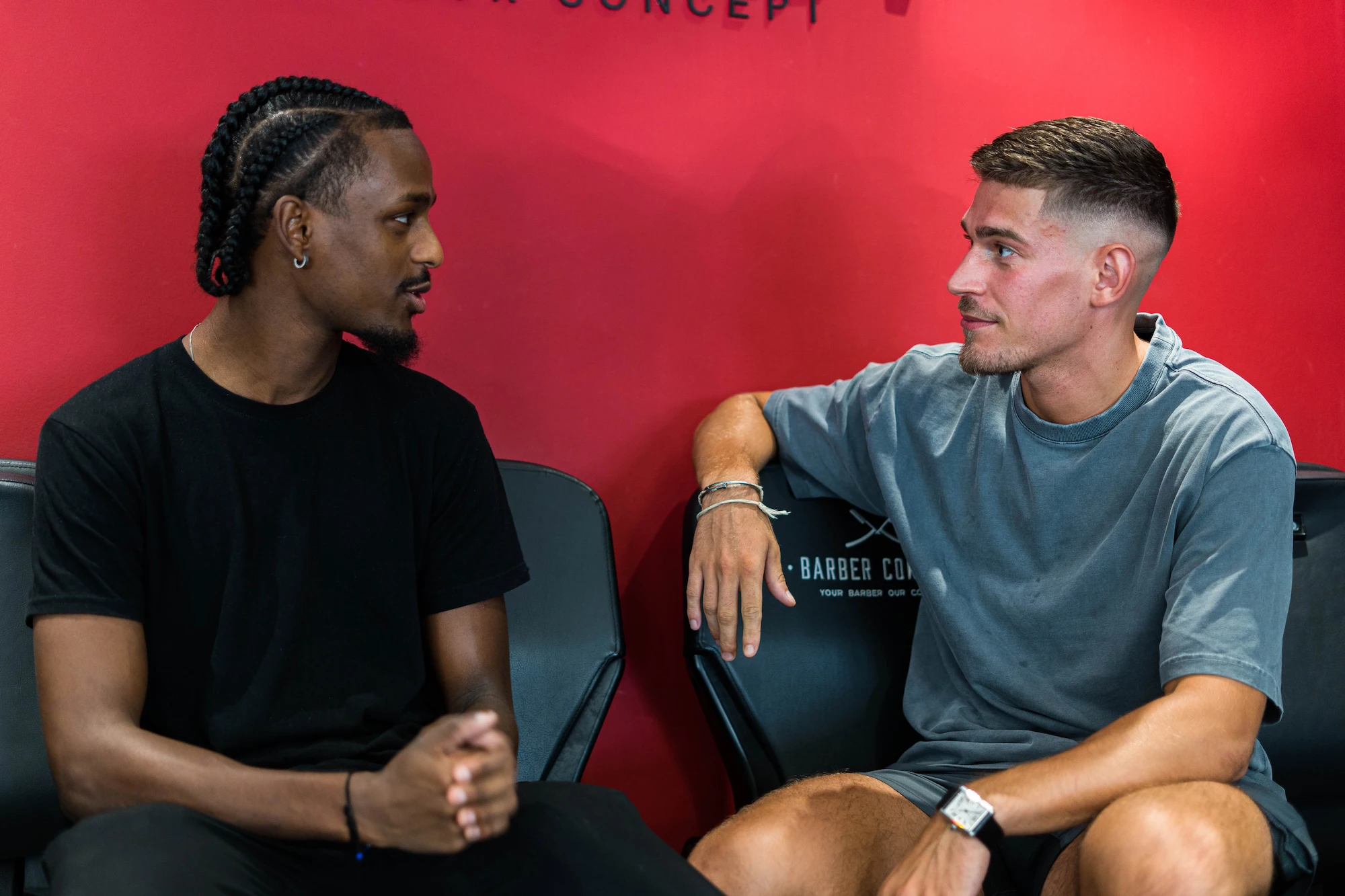 Deux barbiers Barber Concept en discussion devant le mur rouge du salon